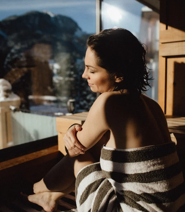 Premium-Spa im Wellnesshotel in Kitzbühel Frau entspannt in Handtuch vor Panoramafenster mit Bergblick