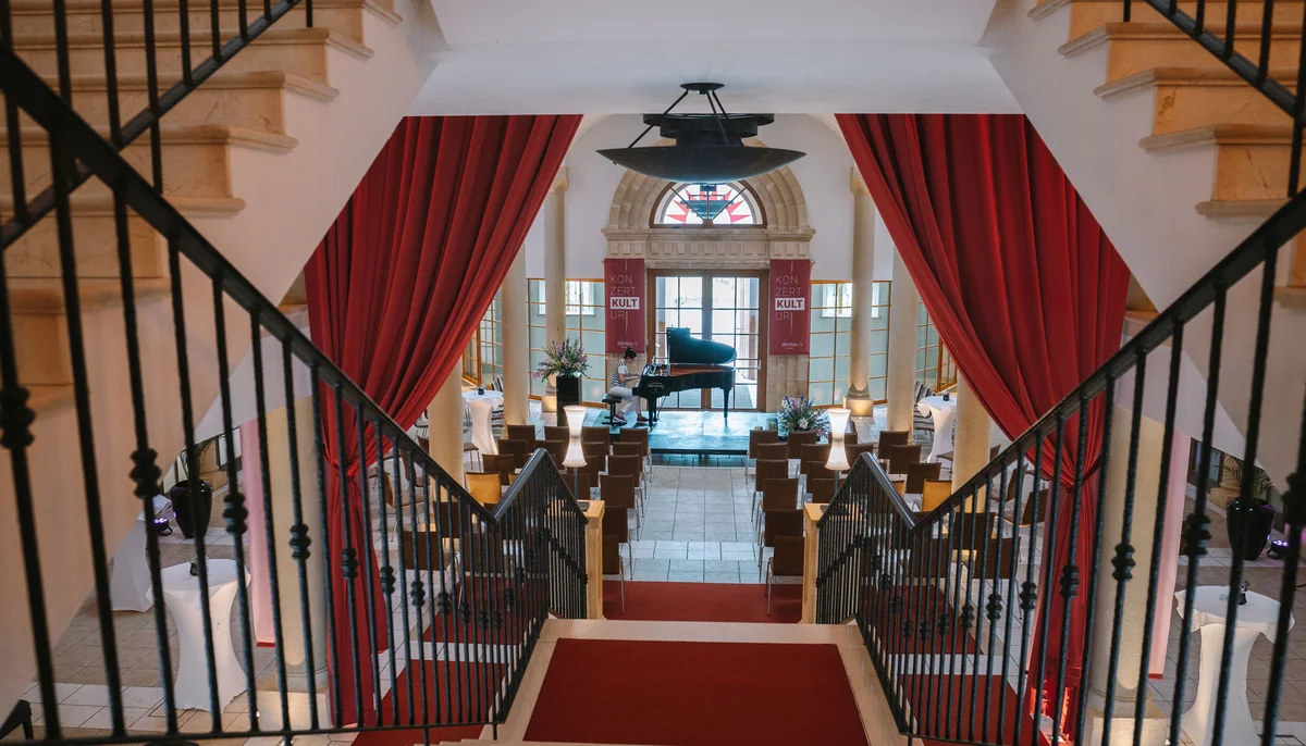 Ihr Firmenevent oder Meeting im Schlosshotel Kitzbühel Blick von Treppe auf Konzertsaal mit Flügel und roten Vorhängen