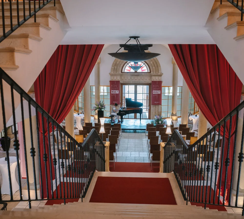 Ihr Firmenevent oder Meeting im Schlosshotel Kitzbühel Blick von Treppe auf Konzertsaal mit Flügel und roten Vorhängen