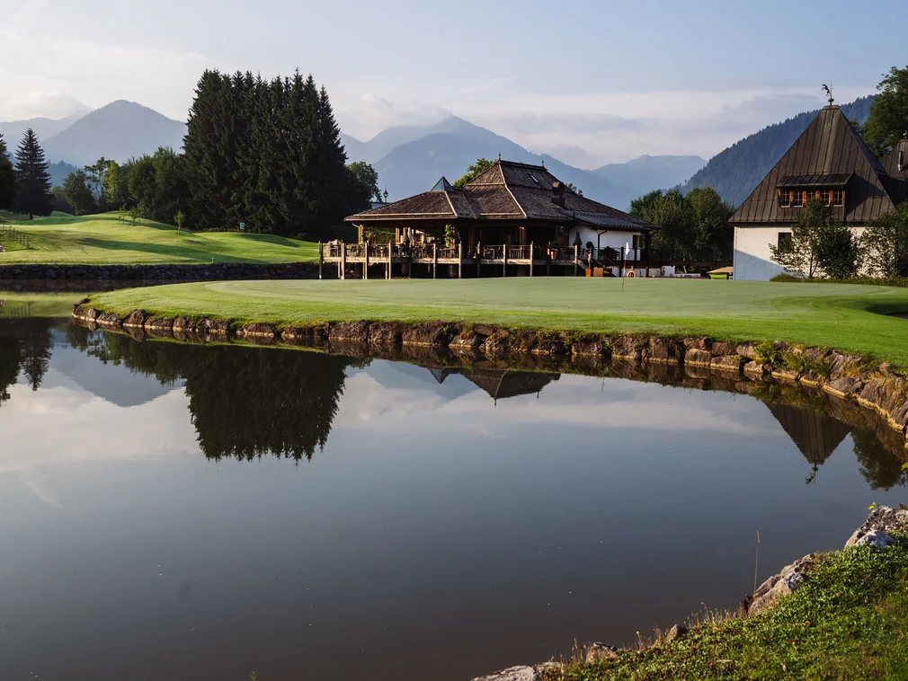 Bilder, die Sie sehen müssen. Golfplatz mit Teich, Bäumen, Clubhaus und Bergen im Hintergrund