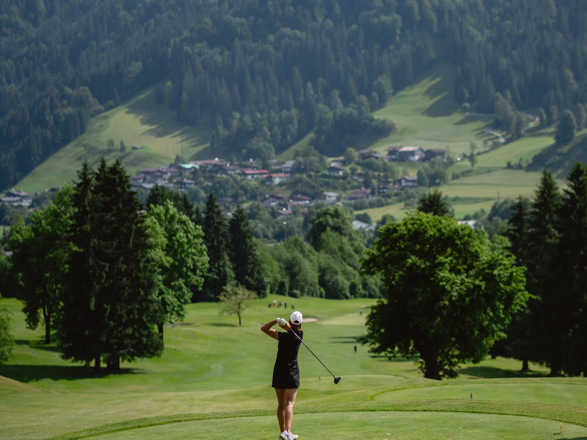 Bilder, die Sie sehen müssen. Golferin schlägt Ball auf grüner Wiese mit Bergkulisse im Hintergrund