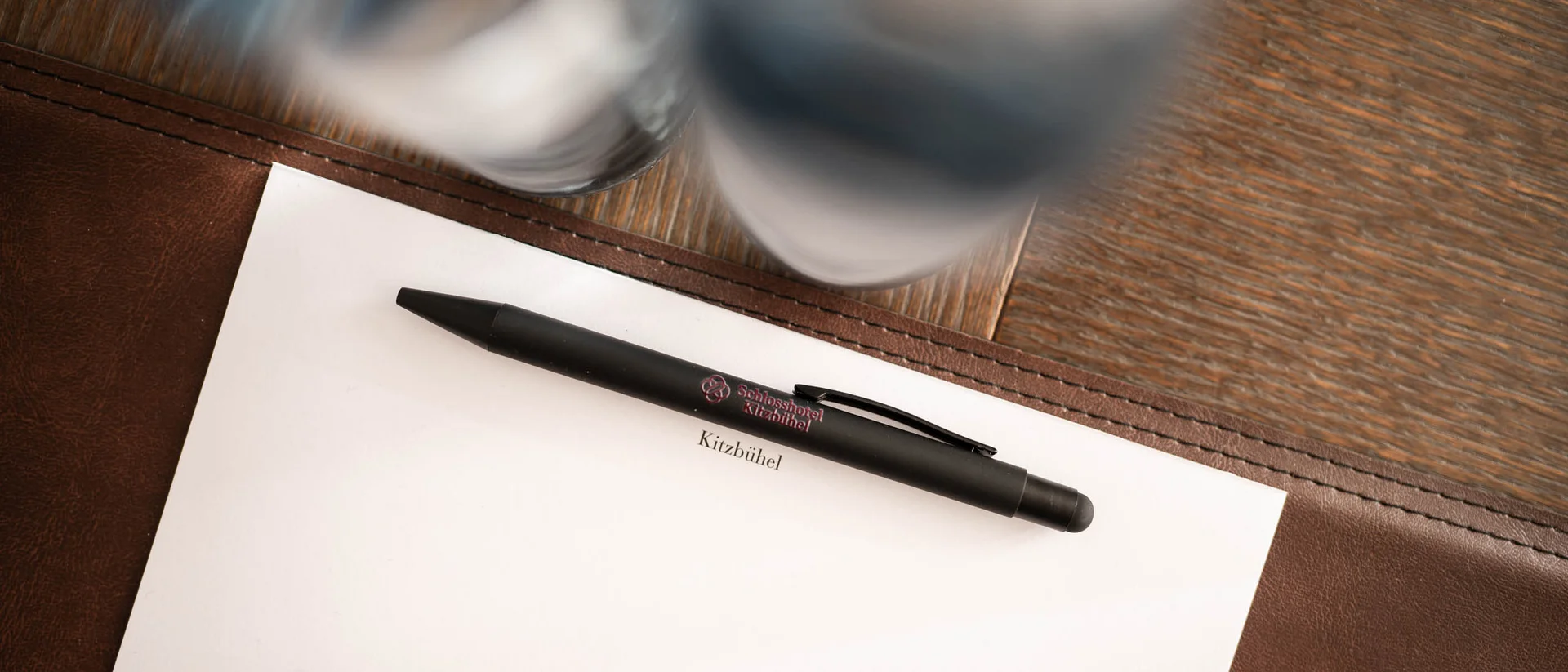 Exklusiv tagen im Seminarhotel in Tirol Schwarzer Stift auf weißem Papier mit Kitzbühel-Schriftzug auf Holztisch