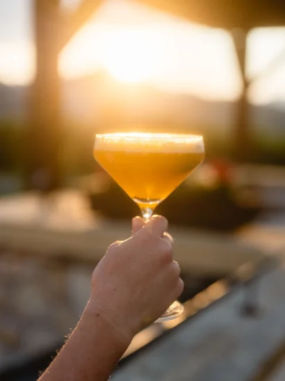 Hotel mit Klavier und Livemusik | Die Bar im Schlosshotel Kitzbühel Hand hält gelb-orangefarbenen Cocktailglas bei Sonnenuntergang