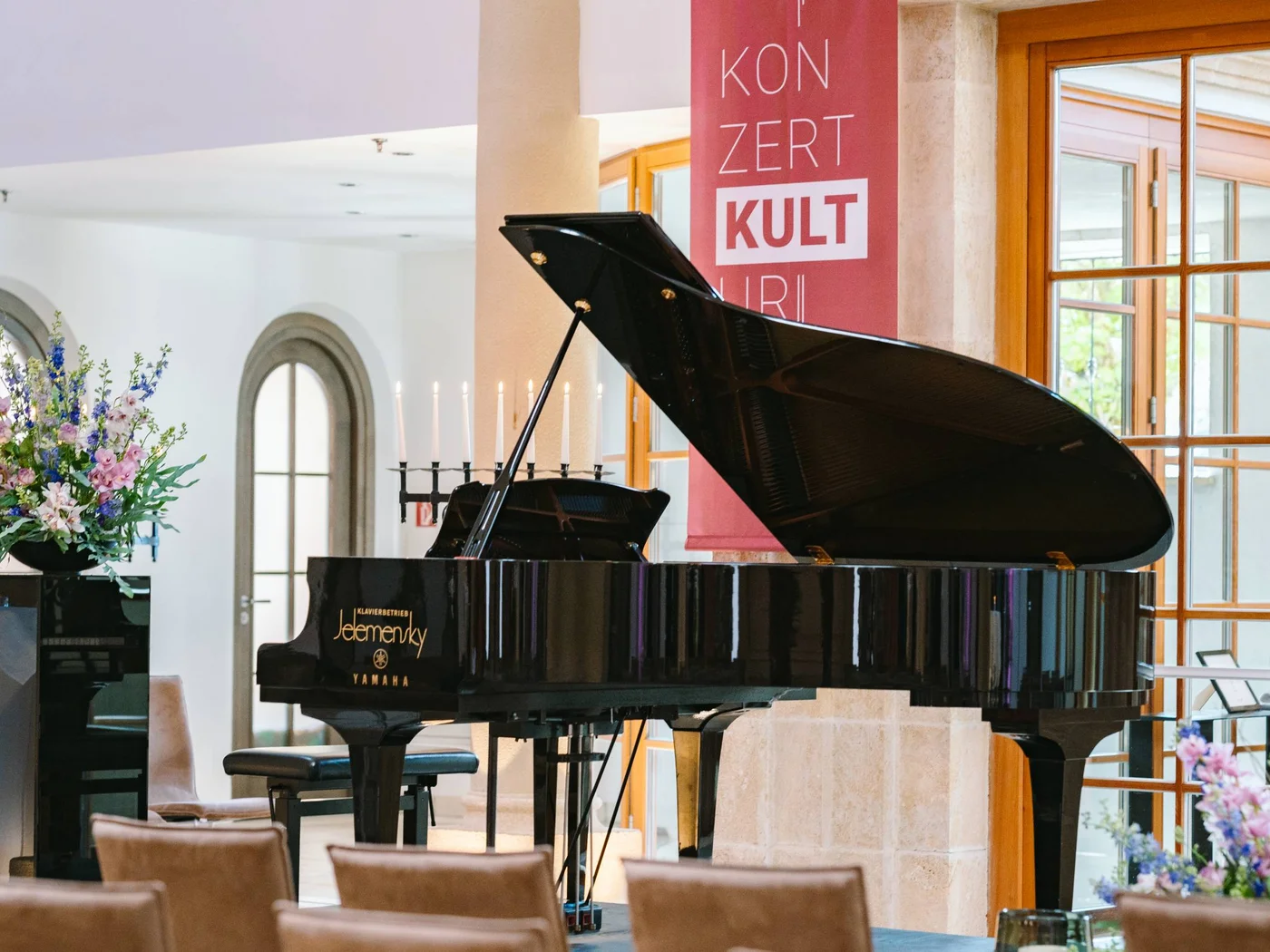 Die Schlossevents Schwarzer Flügelpiano in einem eleganten Raum mit Blumen und Stühlen