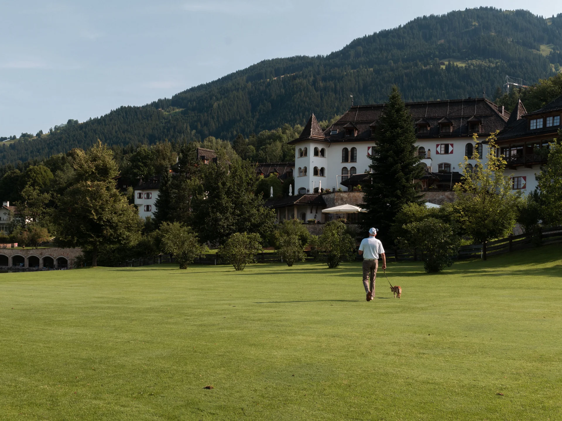 Bilder, die Sie sehen müssen. Mann geht mit Hund auf einer grünen Wiese vor einem bergigen Schloss