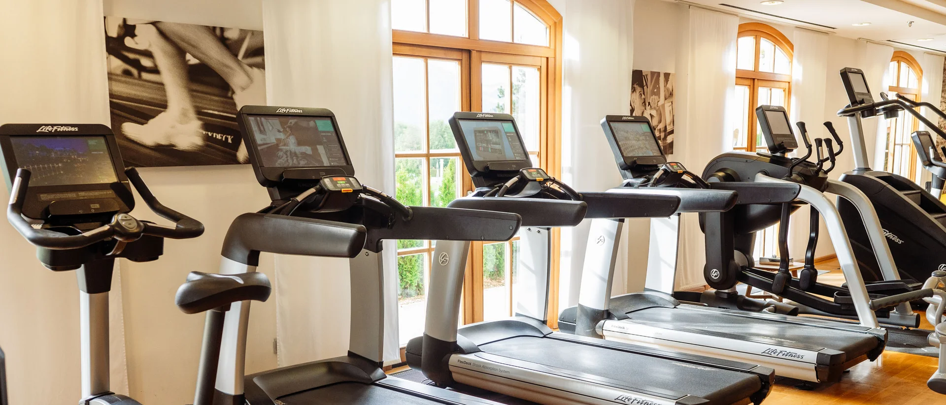 Fitness und Yoga im Hotel in Tirol Fitnessraum mit Laufbändern und Heimtrainern vor großen Fenstern