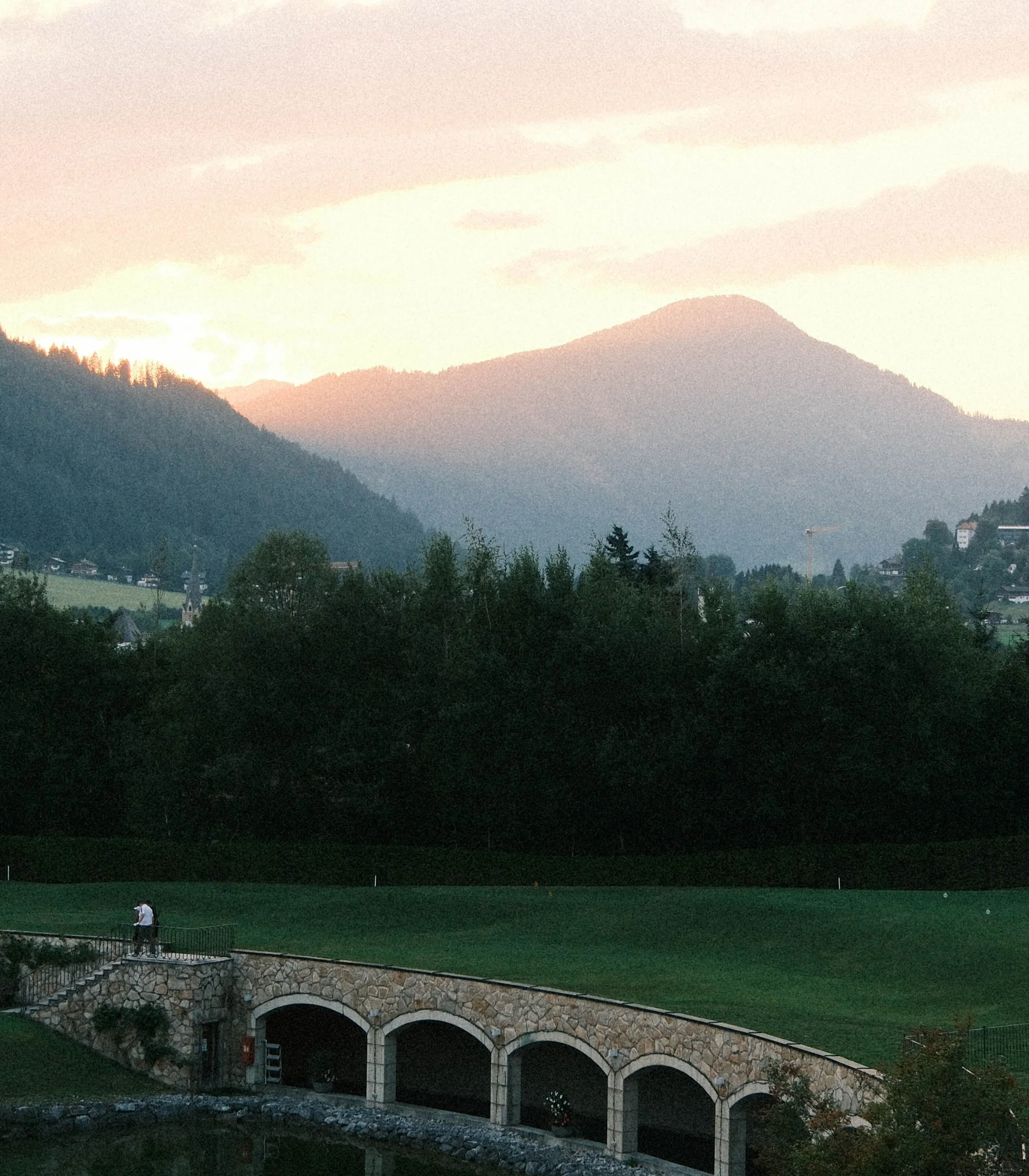Hotel mit Klavier und Livemusik | Die Bar im Schlosshotel Kitzbühel Steinbrücke über kleinen Teich mit bewaldetem Hügel und Bergen im Hintergrund