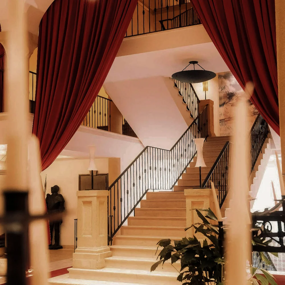Schlosshotel – 5 Sterne in Kitzbühel Elegante Treppe mit schmiedeeisernem Geländer und roten Vorhängen in warm beleuchtetem Raum
