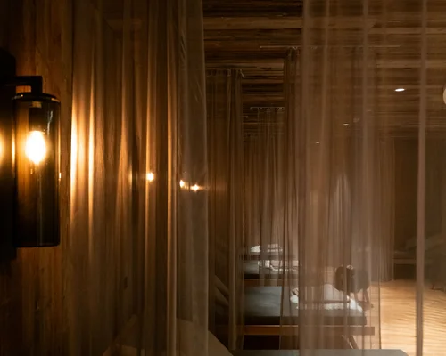 Übernachten in Kitzbühel – Zimmer und Suiten im Schlosshotel Dunkler Raum mit Betten hinter transparenten Vorhängen und warmem Wandlicht