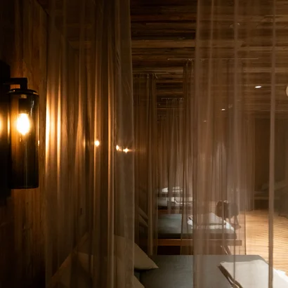 Eine der schönsten Hochzeitslocations in Tirol Dunkler Raum mit Betten hinter transparenten Vorhängen und warmem Wandlicht