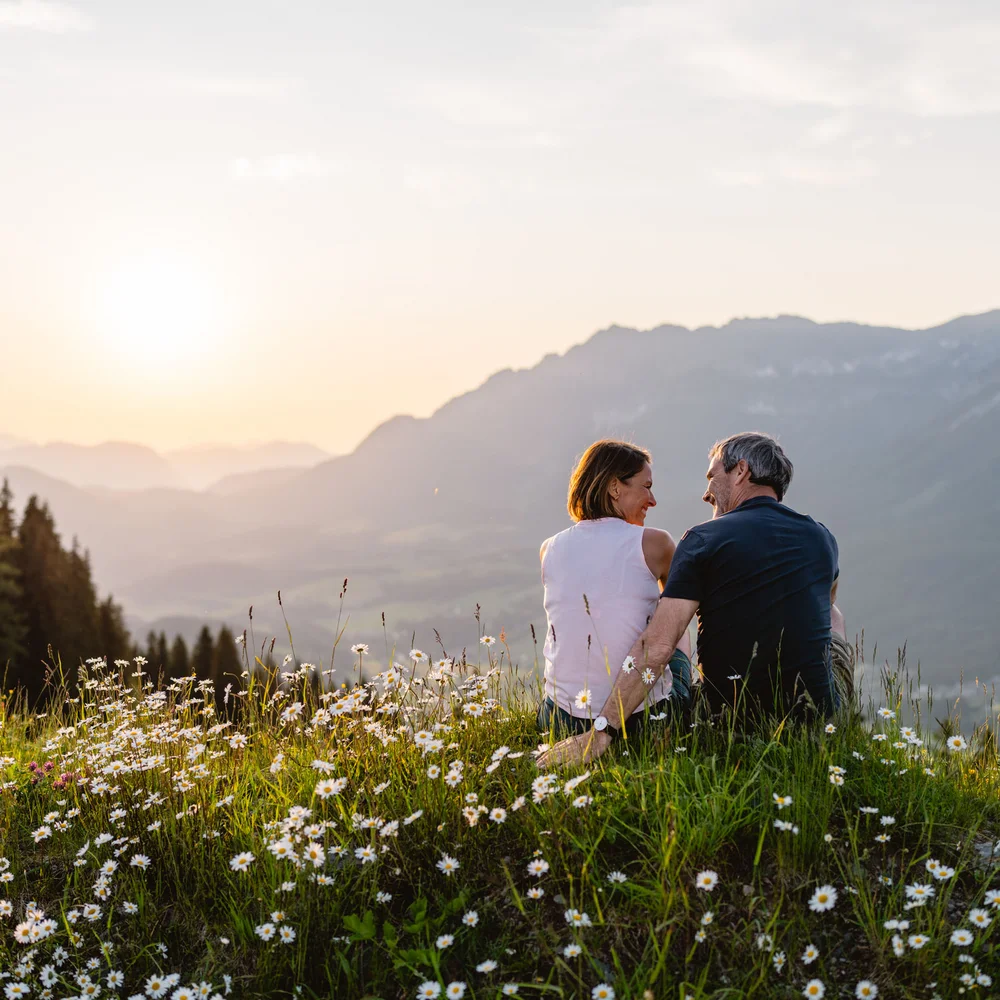 Rund ums Bikehotel in Kitzbühel wandern Paar sitzt auf blumenreicher Wiese und genießt Sonnenuntergang in den Bergen