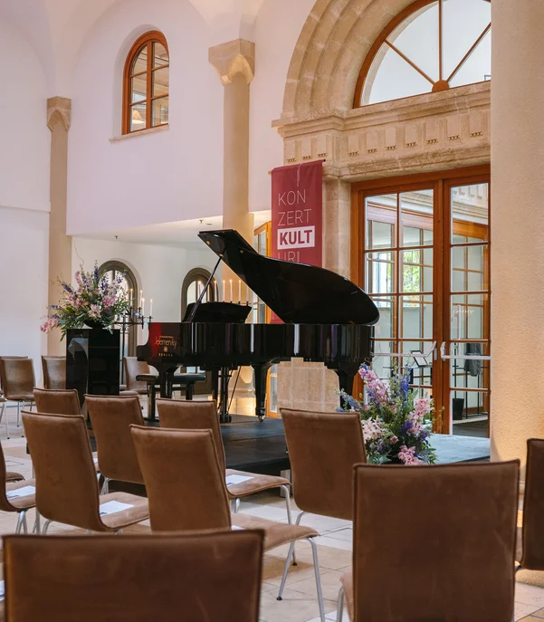Kulturhotel. Schlosshotel. Kitzbühel. Leeres Konzertsaal mit Flügel und Stühlen in elegantem Raum mit Bögen