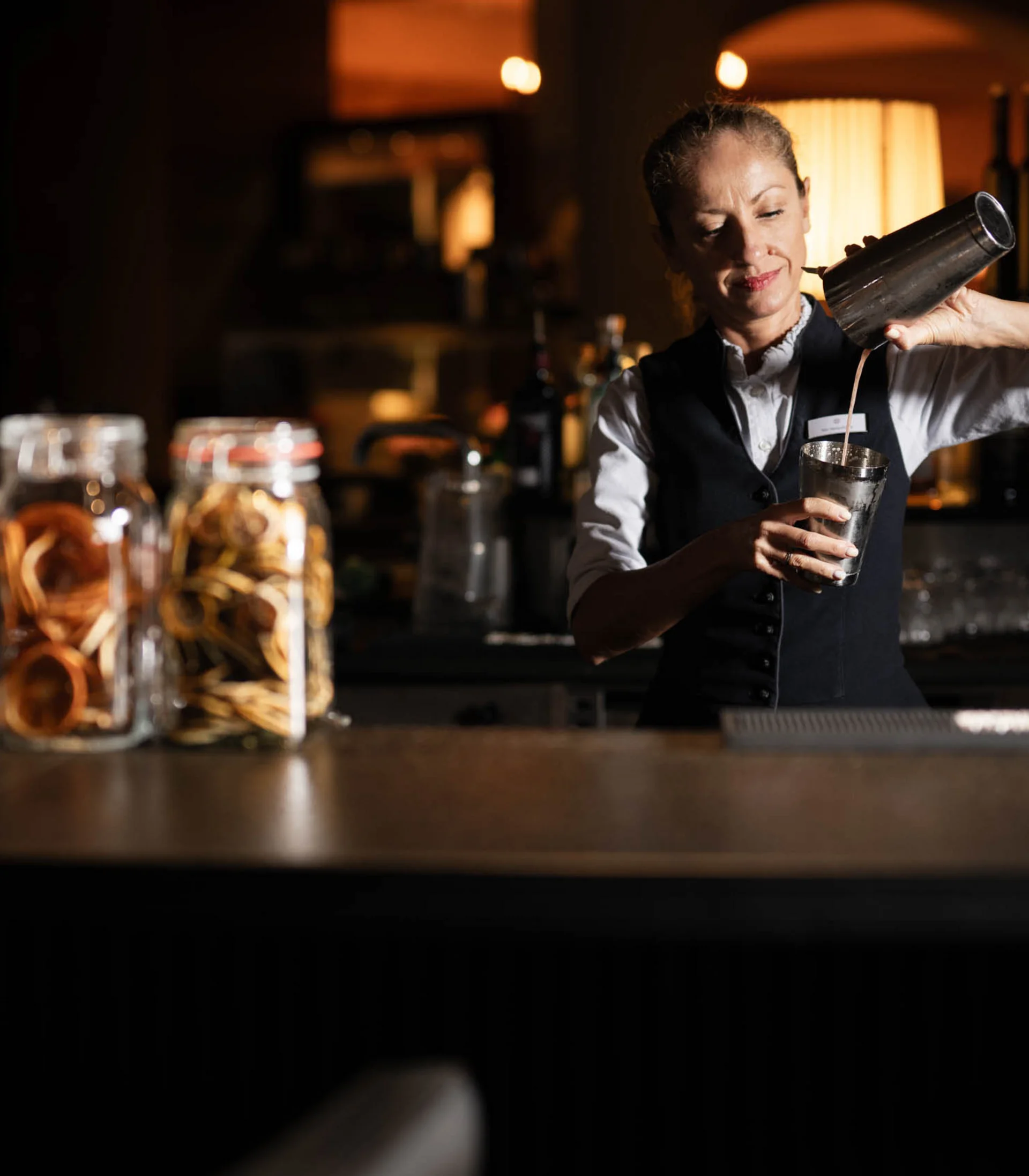 Hotel mit Klavier und Livemusik | Die Bar im Schlosshotel Kitzbühel Bartenderin gießt Getränk mit Shaker in Bar ein