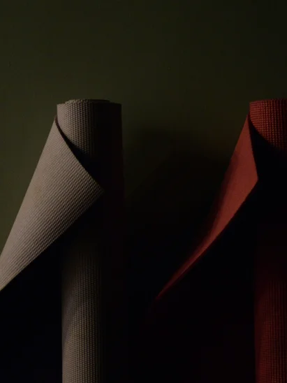 Fitness und Yoga im Hotel in Tirol Zwei zusammengerollte Yogamatten in Grau und Rot vor dunklem Hintergrund