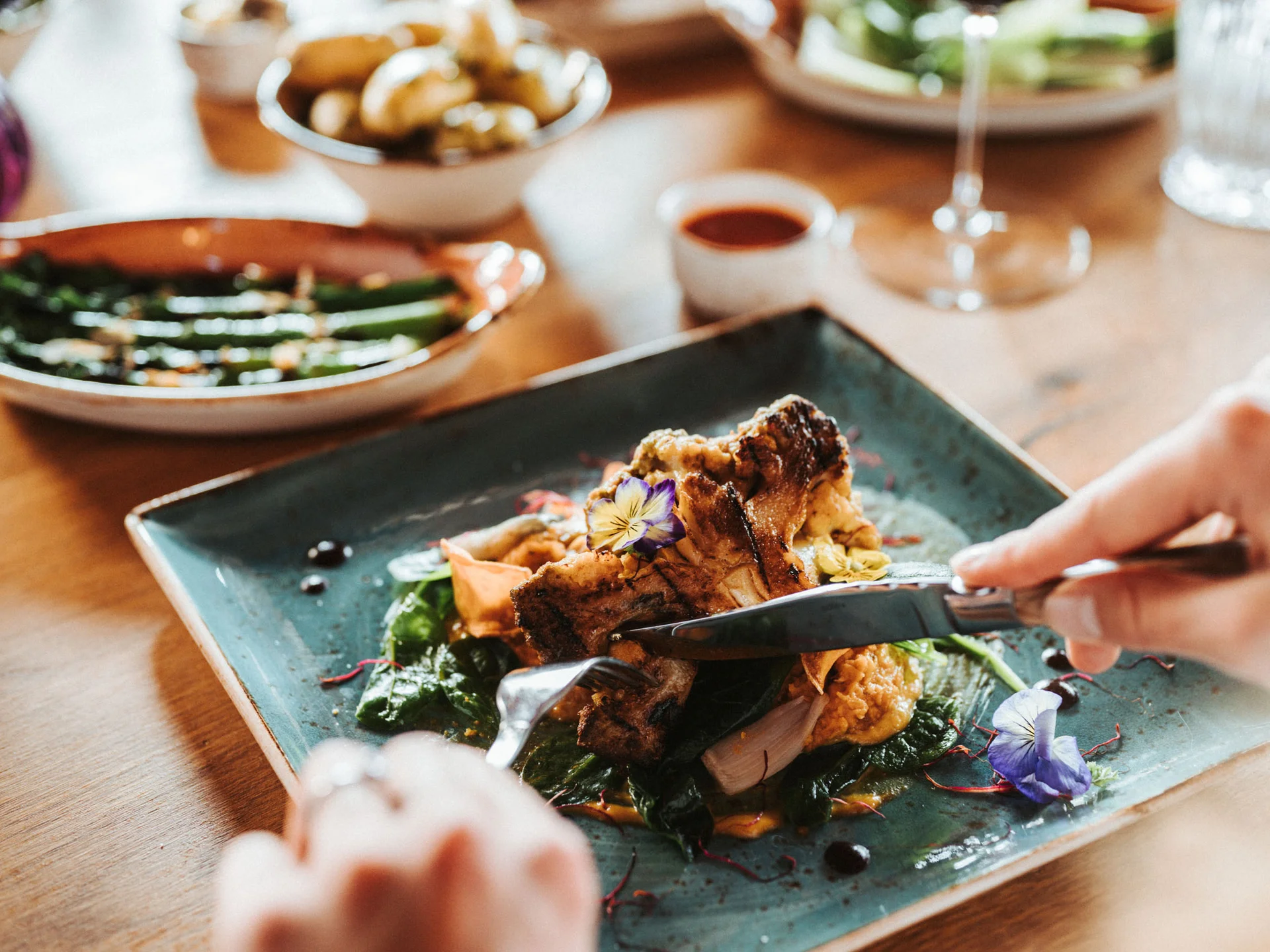 Bilder, die Sie sehen müssen. Person schneidet ein kunstvoll angerichtetes Gericht auf einem blauen Teller