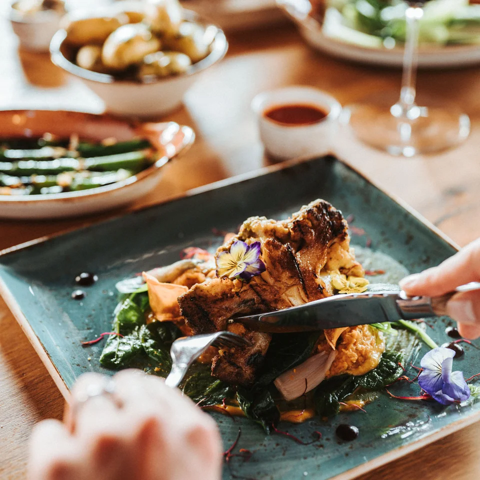 Exklusiv tagen im Seminarhotel in Tirol Person schneidet ein kunstvoll angerichtetes Gericht auf einem blauen Teller