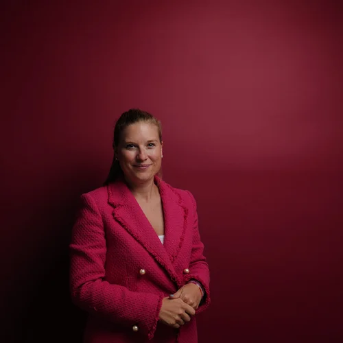 Ihr Firmenevent oder Meeting im Schlosshotel Kitzbühel Frau mit pinkem Blazer vor rotem Hintergrund lächelnd