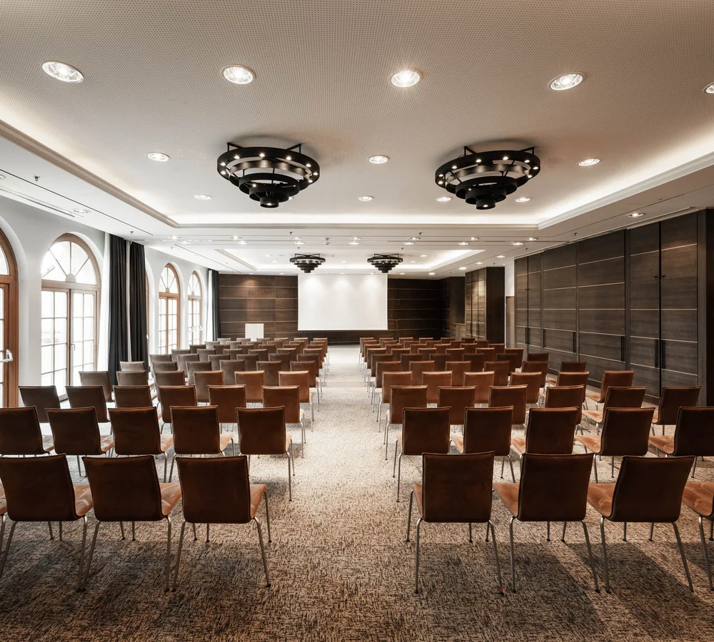 Ihr Firmenevent oder Meeting im Schlosshotel Kitzbühel Leerer moderner Konferenzraum mit Reihen von Stühlen und Projektionsleinwand