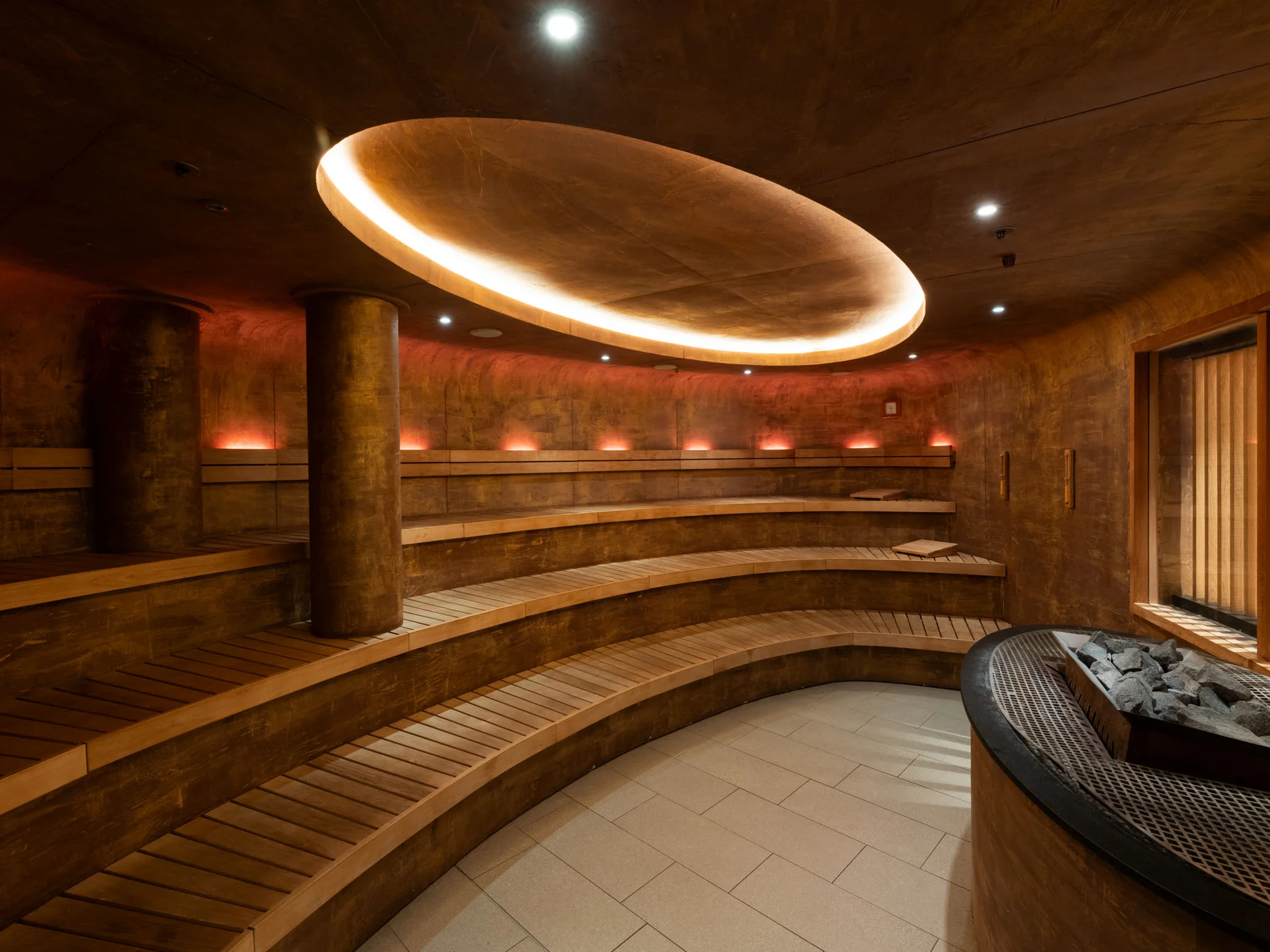 Bilder, die Sie sehen müssen. Moderner, runder Saunaraum mit Holzliegen und indirekter Deckenbeleuchtung