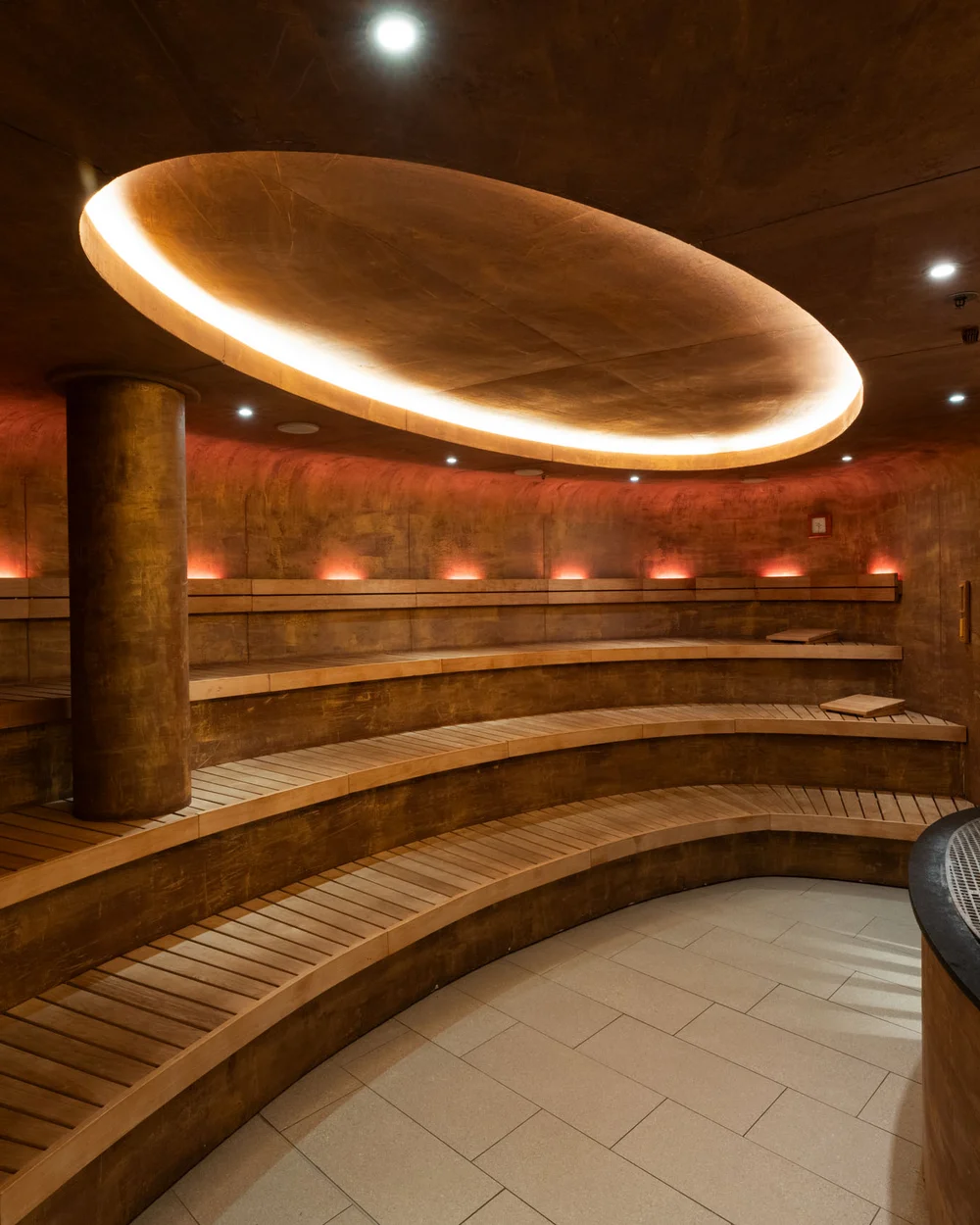 In Kitzbühel ein Hotel mit Pool, bitte. Moderner, runder Saunaraum mit Holzliegen und indirekter Deckenbeleuchtung