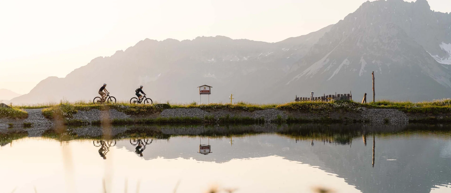 Ein ganzes Jahr in Bewegung Zwei Radfahrer fahren entlang eines Sees mit Bergen im Hintergrund bei Sonnenuntergang