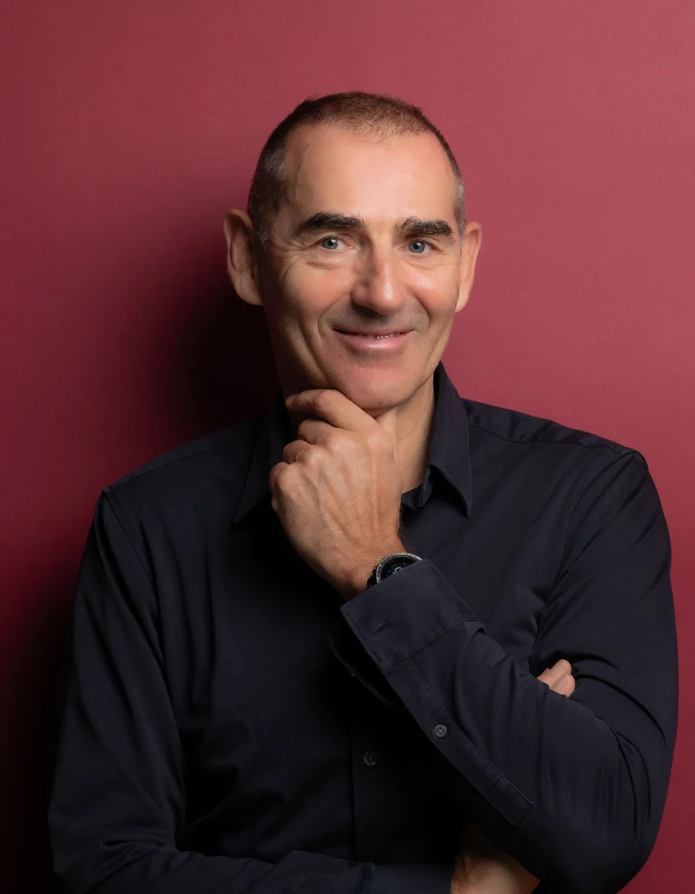 Was zählt, sind die Menschen. Älterer Mann in schwarzem Hemd vor rotem Hintergrund, der nachdenklich lächelt