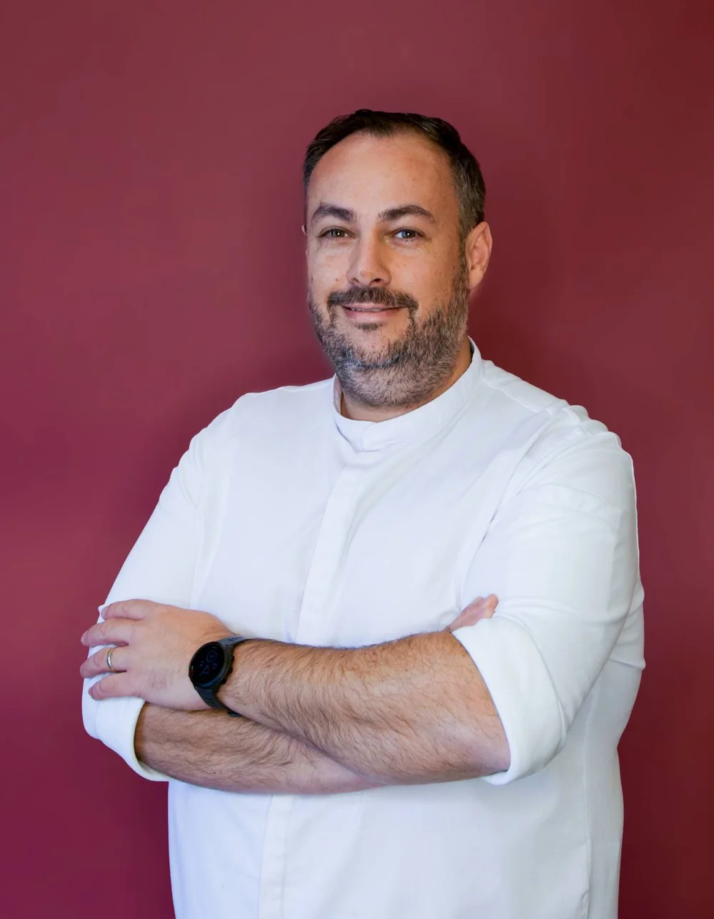 Was zählt, sind die Menschen. Mann mit weißem Hemd und Uhr vor rotem Hintergrund blickt in die Kamera