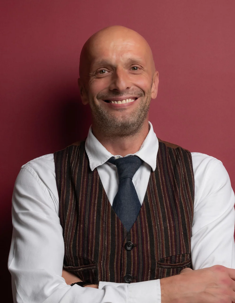 Was zählt, sind die Menschen. Lächelnder Mann mit Hemd, Weste und Krawatte vor rotem Hintergrund