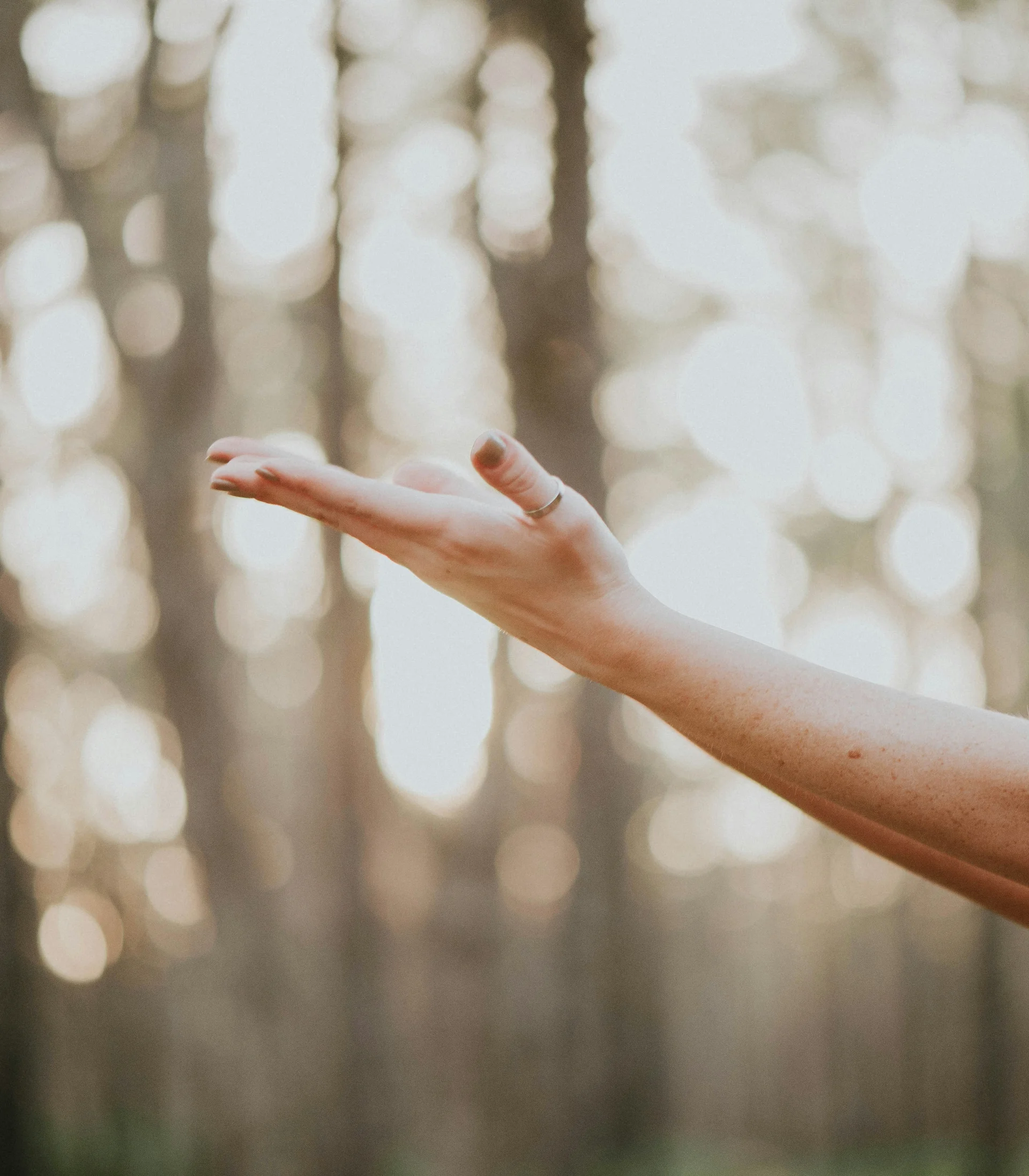 Fitness und Yoga im Hotel in Tirol Ausgestreckter Arm mit offener Hand vor verschwommenem Wald im Hintergrund