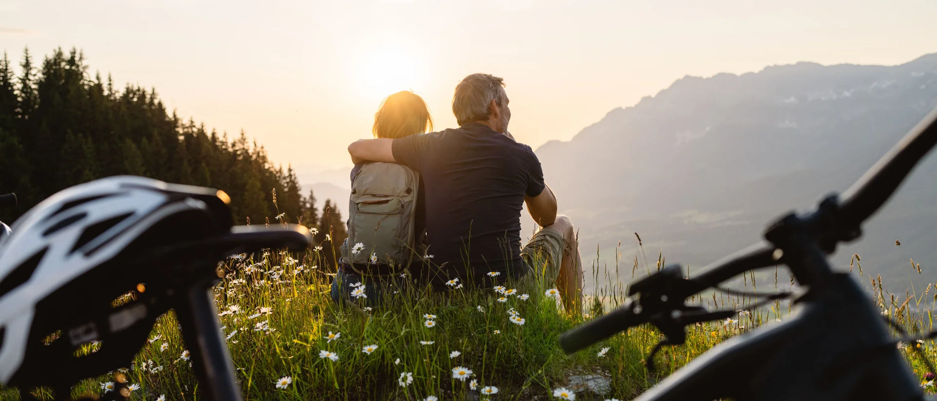 Rund ums Bikehotel in Kitzbühel wandern Paar sitzt auf einer Wiese mit Blumen und blickt auf Berge im Sonnenuntergang