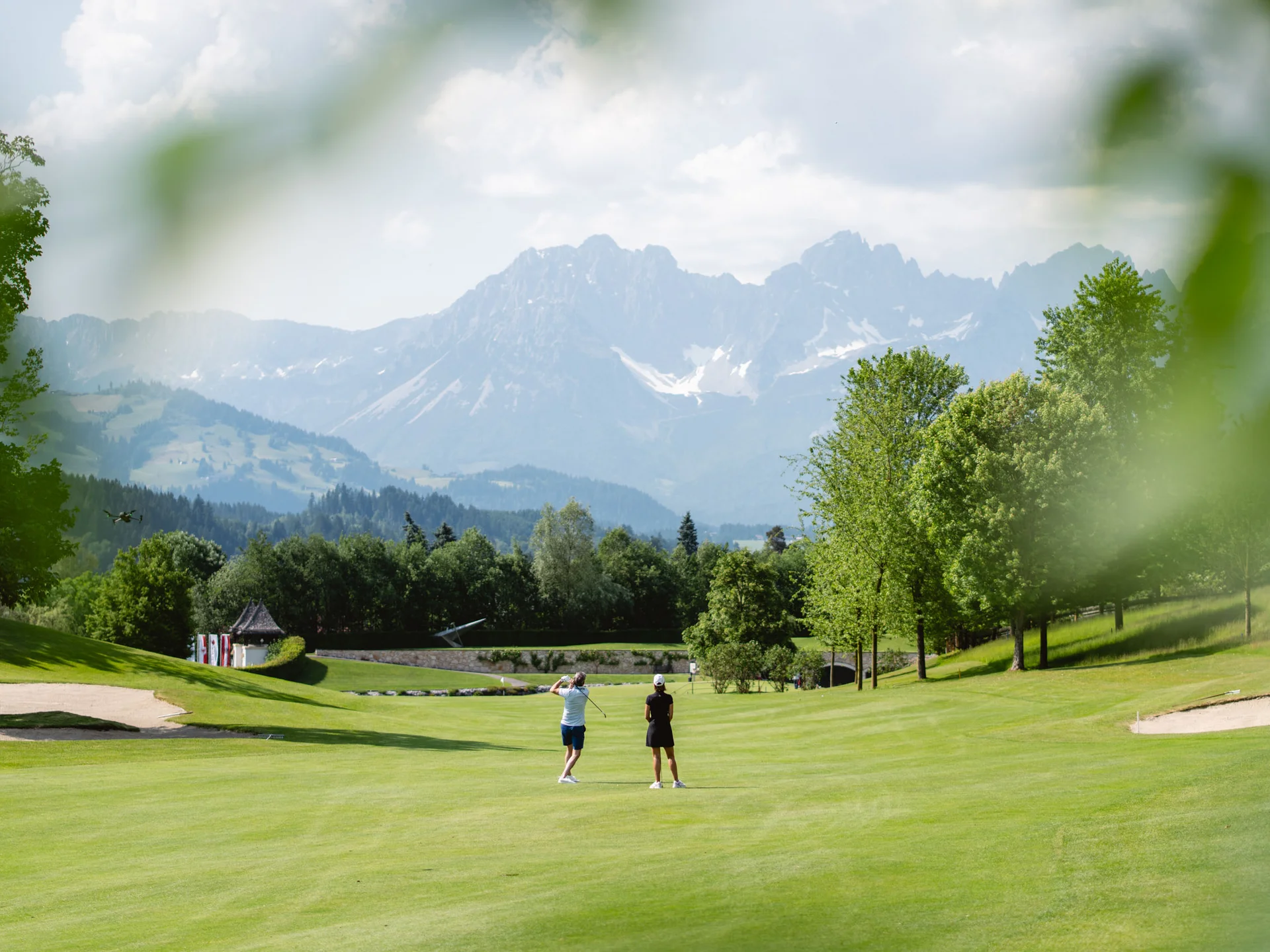 Bilder, die Sie sehen müssen. Zwei Golfer auf grünem Golfplatz mit Bergen im Hintergrund bei sonnigem Wetter