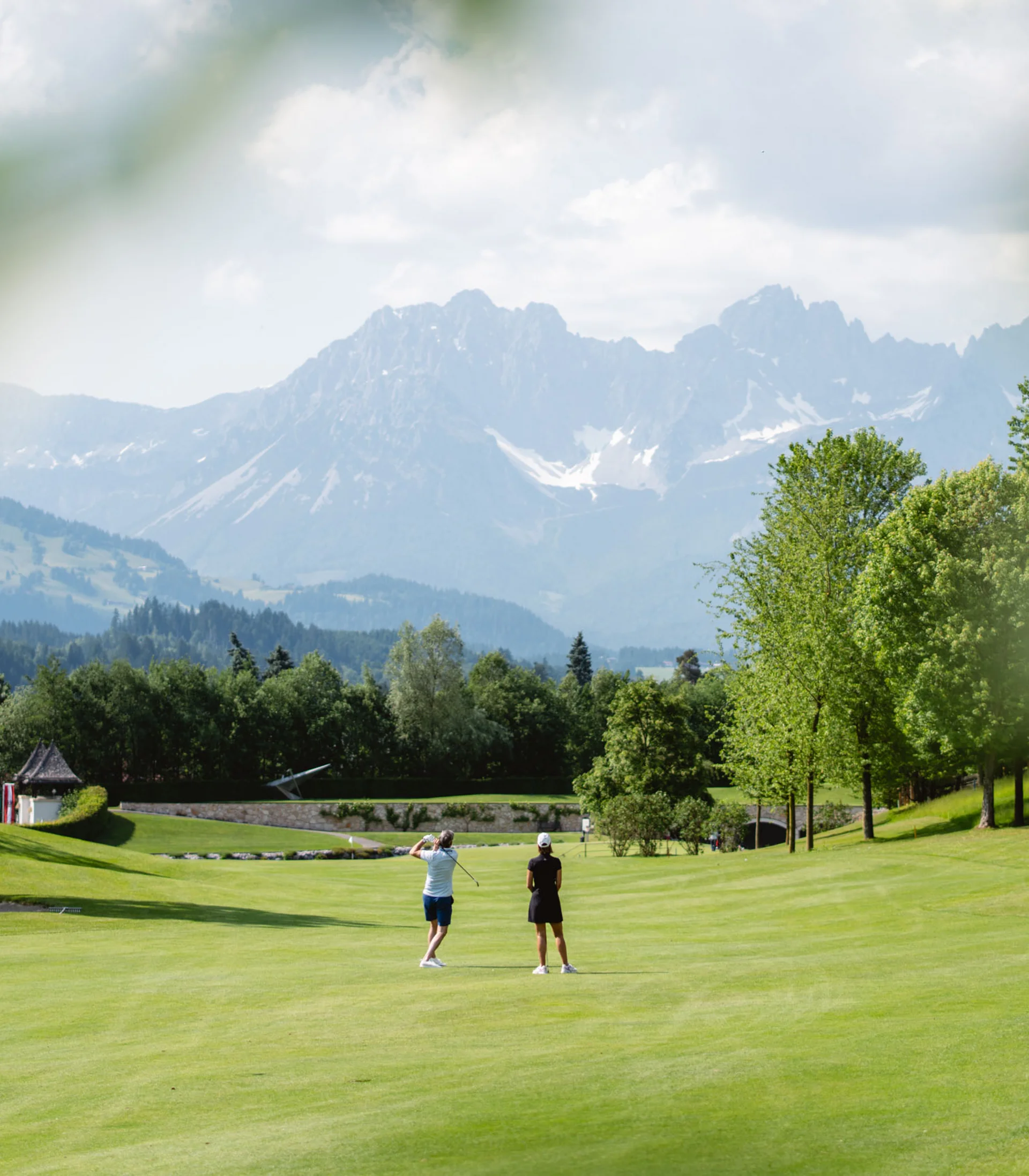 Aktiv in der Gamsstadt im Sporthotel in Kitzbühel Zwei Golfer auf grünem Golfplatz mit Bergen im Hintergrund bei sonnigem Wetter