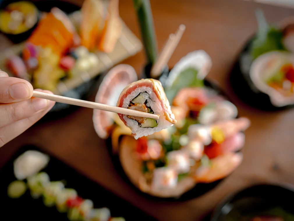 Bilder, die Sie sehen müssen. Hand hält Sushi mit Stäbchen über Platte mit verschiedenen Sushi