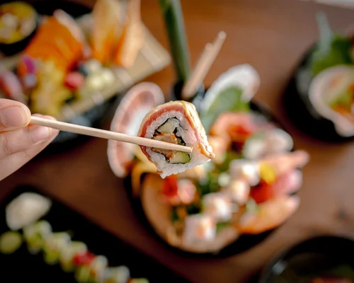 Übernachten in Kitzbühel – Zimmer und Suiten im Schlosshotel Hand hält Sushi mit Stäbchen über Platte mit verschiedenen Sushi