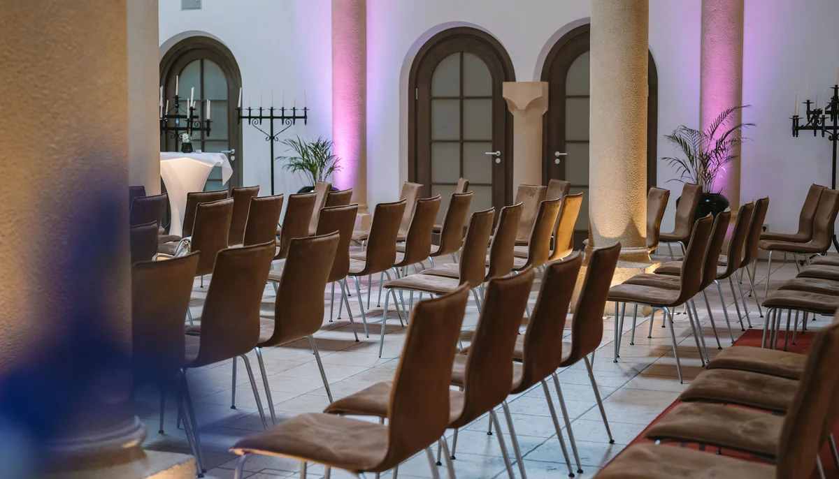 Ihr Firmenevent oder Meeting im Schlosshotel Kitzbühel Leere Stuhlreihen in einem Raum mit Säulen und lila Beleuchtung