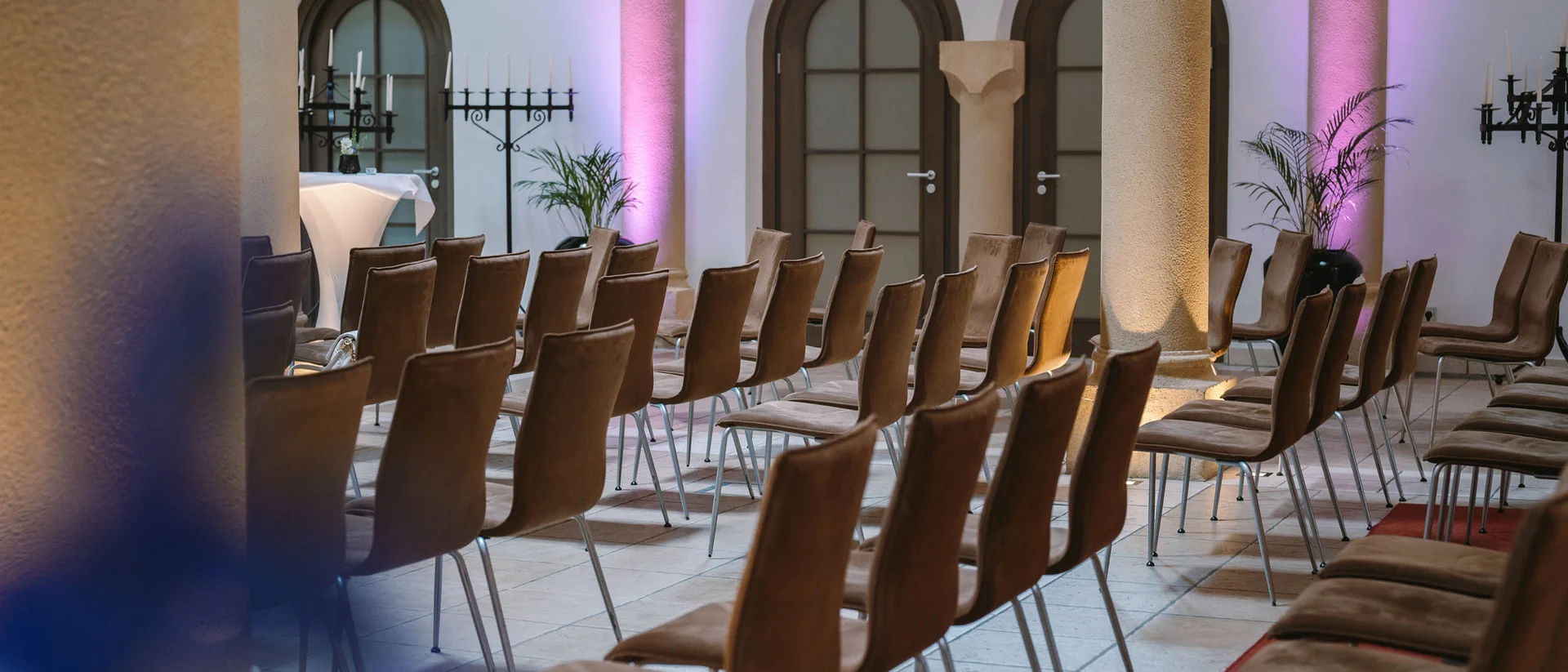 Ihr Firmenevent oder Meeting im Schlosshotel Kitzbühel Leere Stuhlreihen in einem Raum mit Säulen und lila Beleuchtung