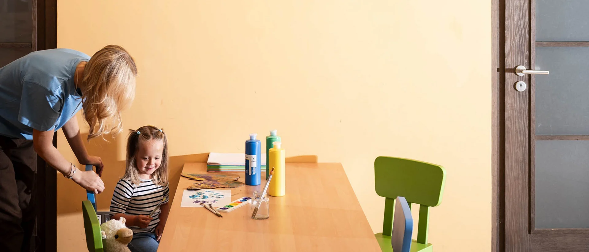 So schön: Kitzbühel-Urlaub mit Kindern Kind sitzt am Tisch mit Farbe, Erwachsene hilft im Raum mit gelben Wänden