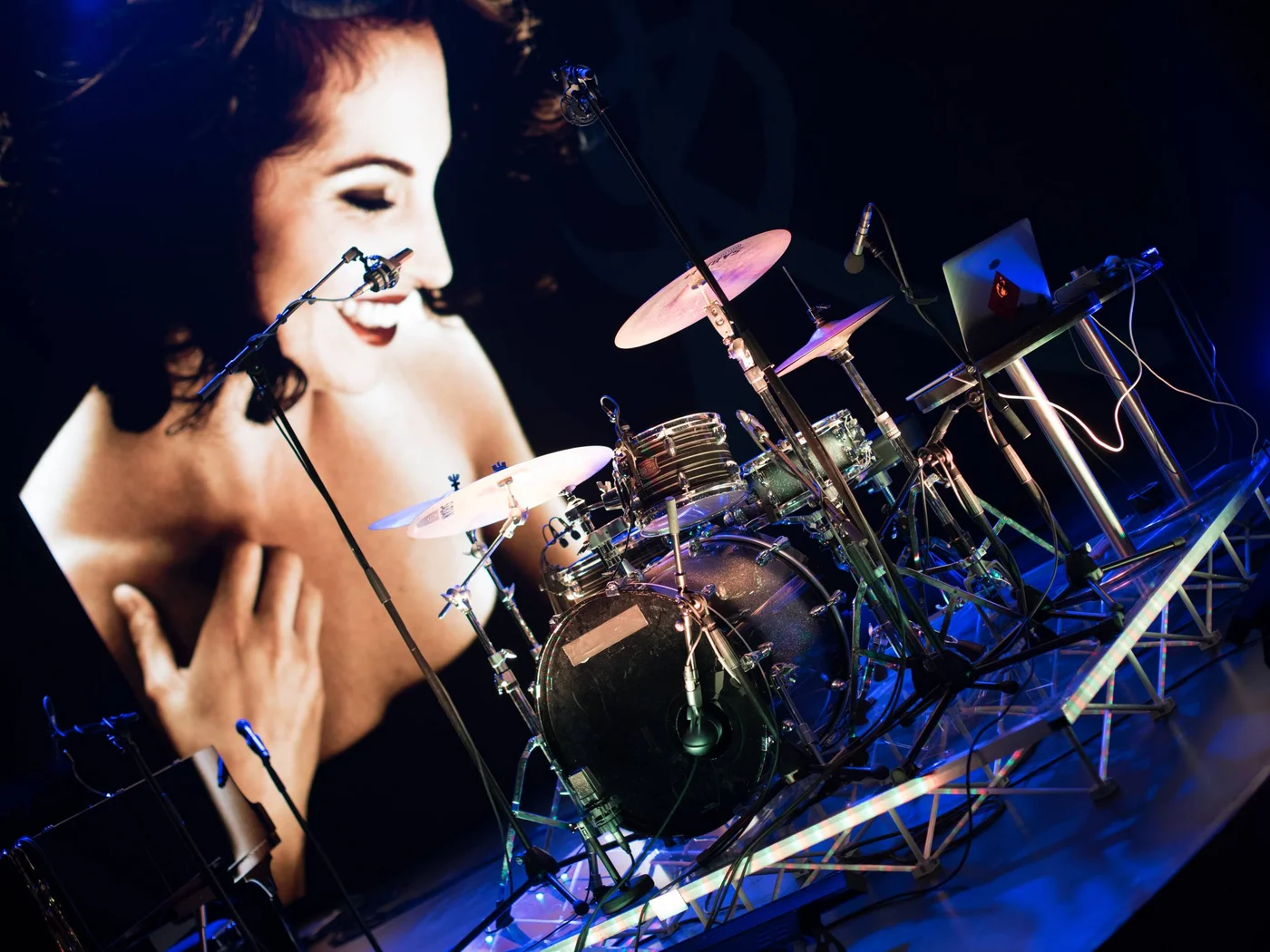 Die Schlossevents Schlagzeug und Mikrofone vor einem großen Bildschirm mit lachender Frau