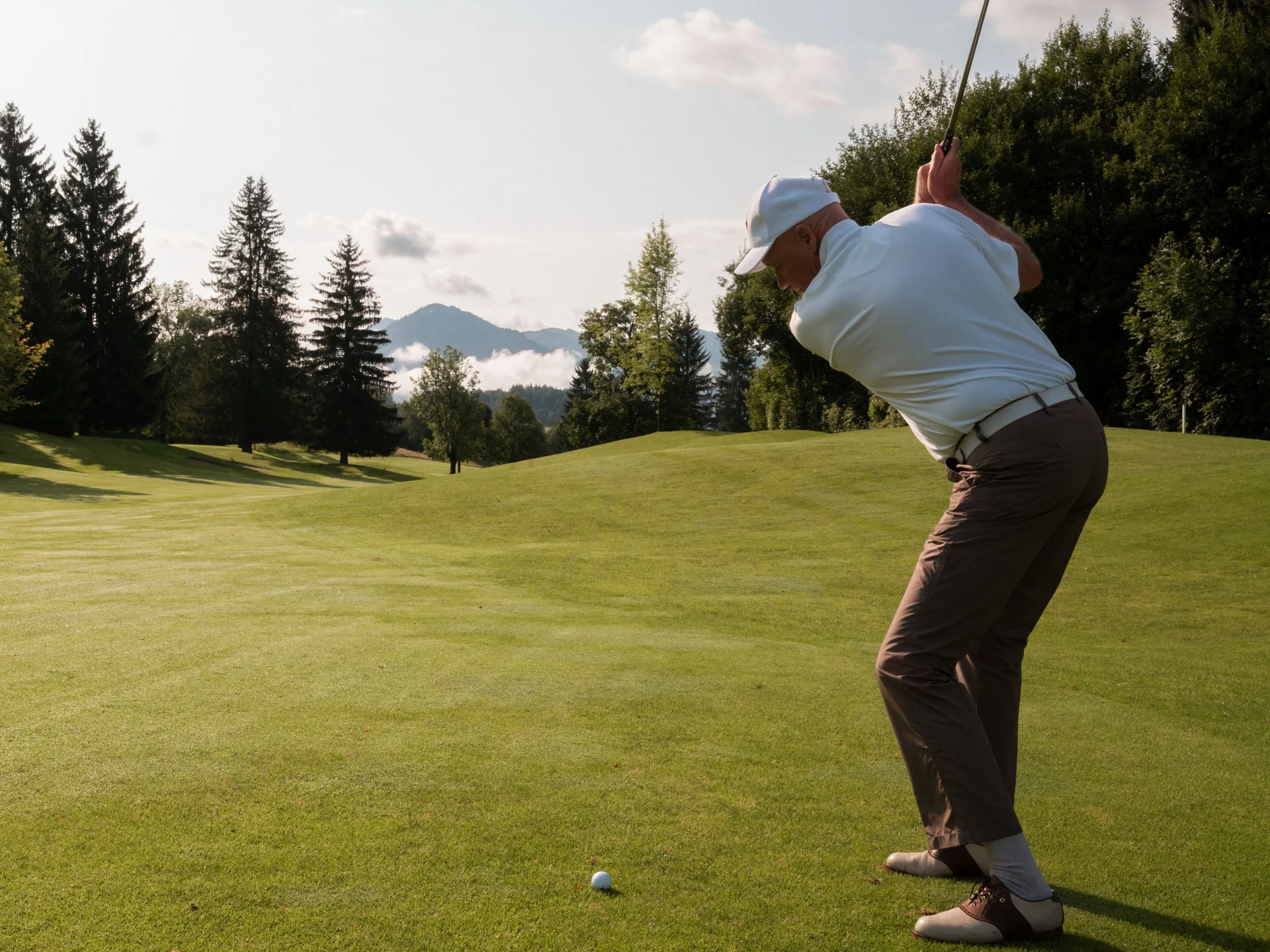 Bilder, die Sie sehen müssen. Mann beim Golfspielen auf einem sonnigen Golfplatz mit Bergen im Hintergrund