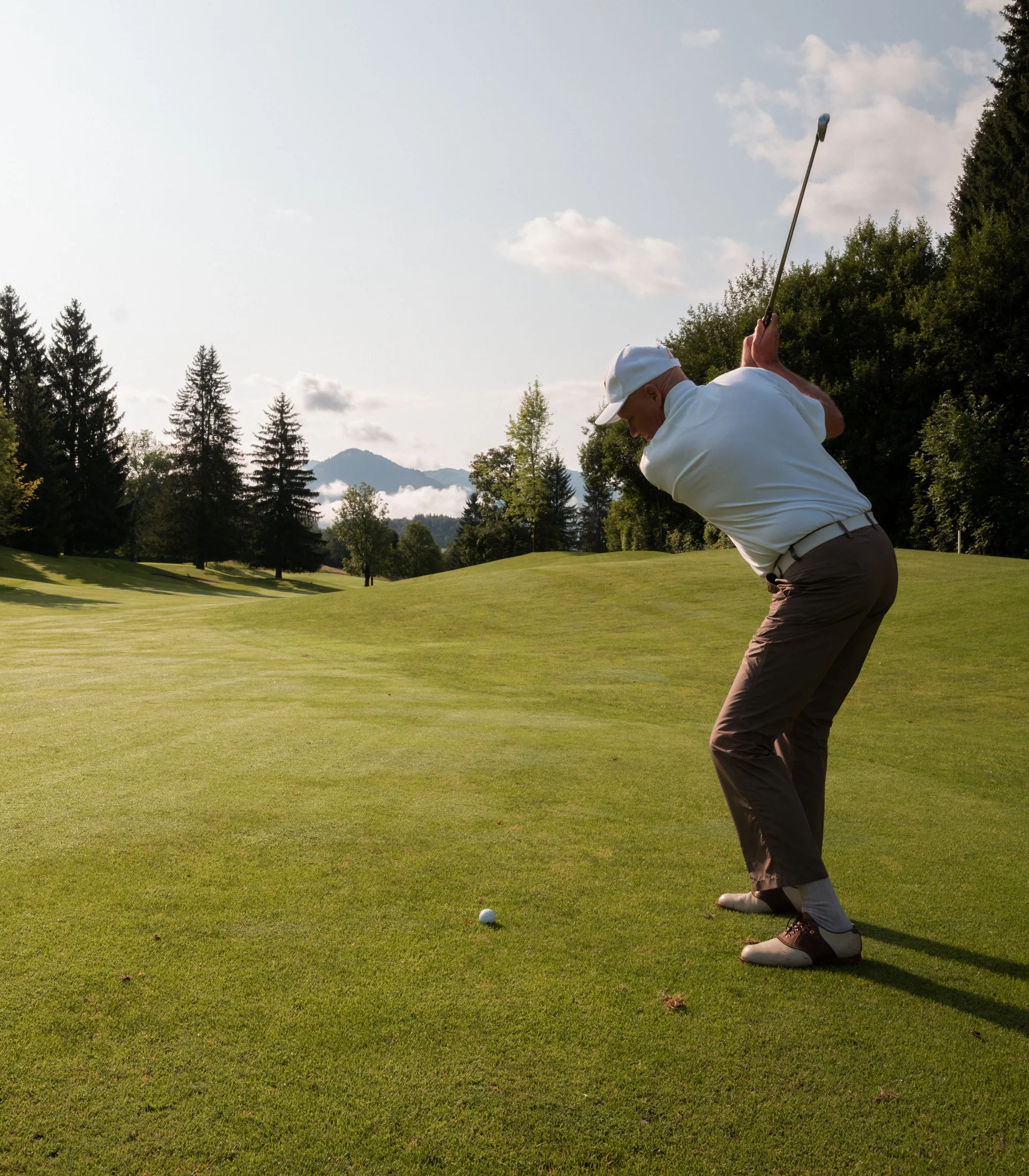 Schlosshotel – 5 Sterne in Kitzbühel Mann beim Golfspielen auf einem sonnigen Golfplatz mit Bergen im Hintergrund