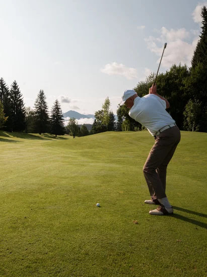 Das Golfhotel in Kitzbühel Mann beim Golfspielen auf einem sonnigen Golfplatz mit Bergen im Hintergrund