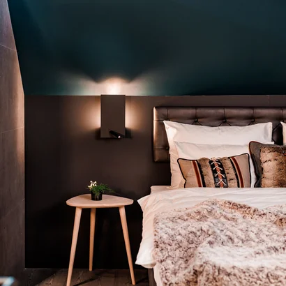 Eine der schönsten Hochzeitslocations in Tirol Gemütliches Schlafzimmer mit dunkler Wand, Holz-Nachttisch und Kissen auf dem Bett