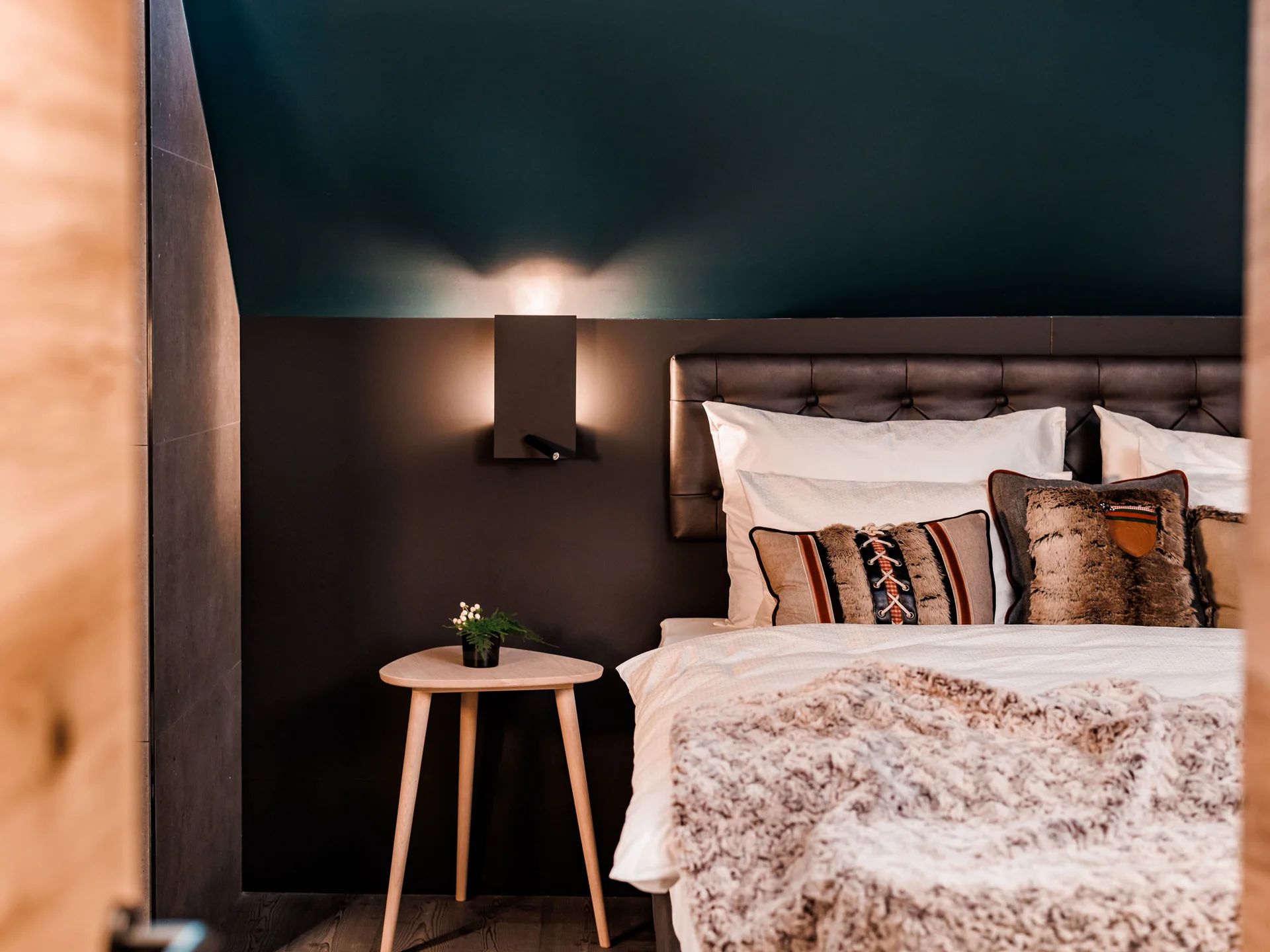 Bilder, die Sie sehen müssen. Gemütliches Schlafzimmer mit dunkler Wand, Holz-Nachttisch und Kissen auf dem Bett