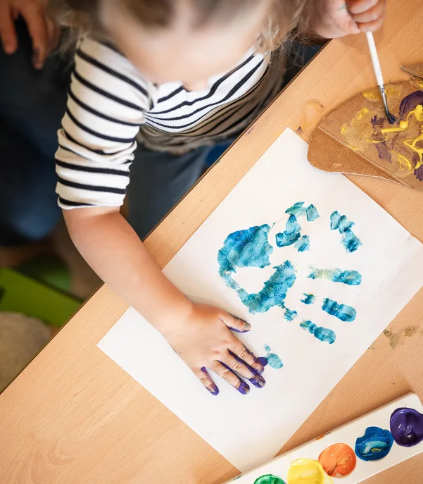 Mit der Familie ins Hotel? Tirol ist die richtige Wahl. Kind macht Handabdruck mit blauer Farbe auf Papier