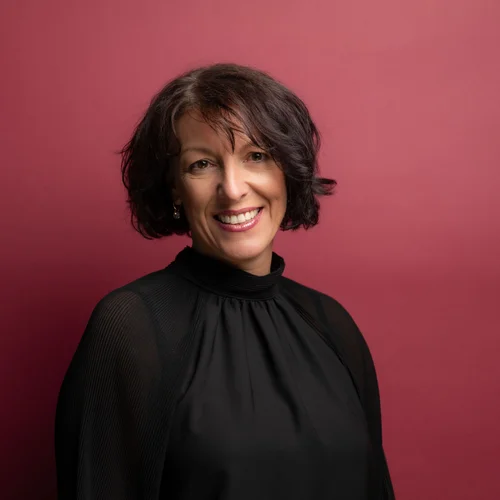 Ihre Karriere im Schlosshotel Kitzbühel Porträt einer lächelnden Frau mit kurzen dunklen Haaren vor rotem Hintergrund