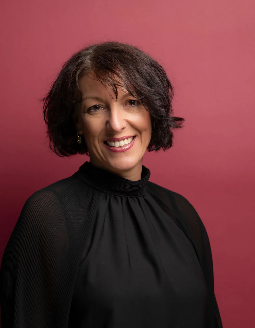 Was zählt, sind die Menschen. Porträt einer lächelnden Frau mit kurzen dunklen Haaren vor rotem Hintergrund