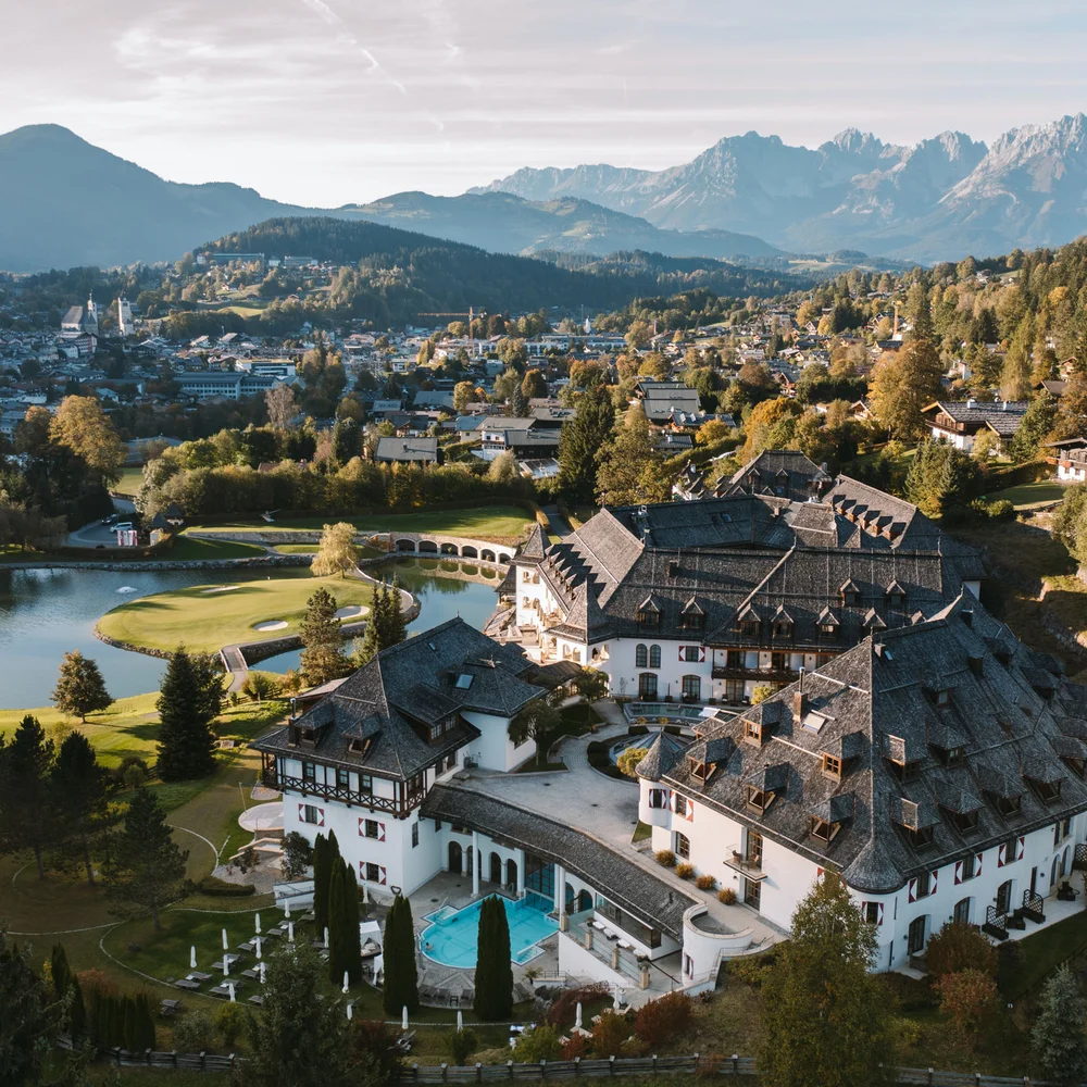 Eine der schönsten Hochzeitslocations in Tirol Luftaufnahme eines Hotels in den Bergen mit Golfplatz und Dorf im Hintergrund