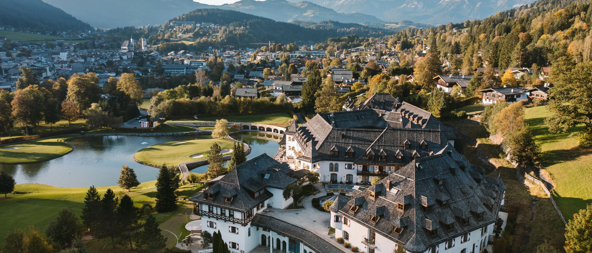 Schlosshotel – 5 Sterne in Kitzbühel Luftaufnahme eines Hotels in den Bergen mit Golfplatz und Dorf im Hintergrund