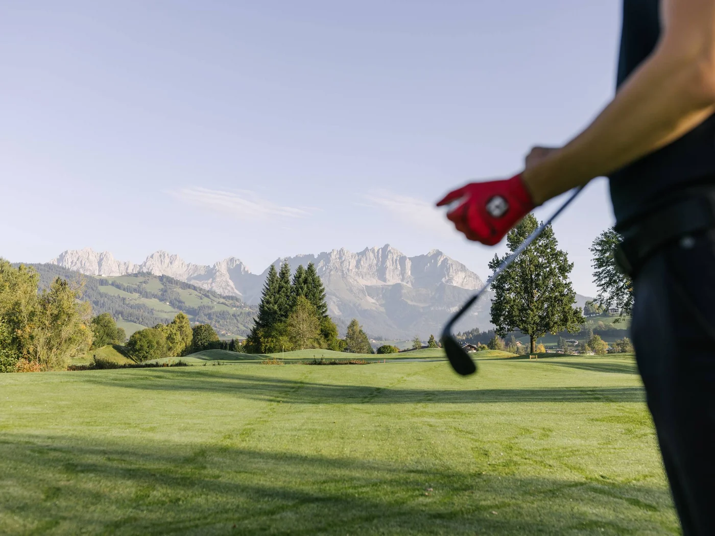 Die Schlossevents Golfer mit rotem Handschuh auf einem grünen Golfplatz vor Bergkulisse