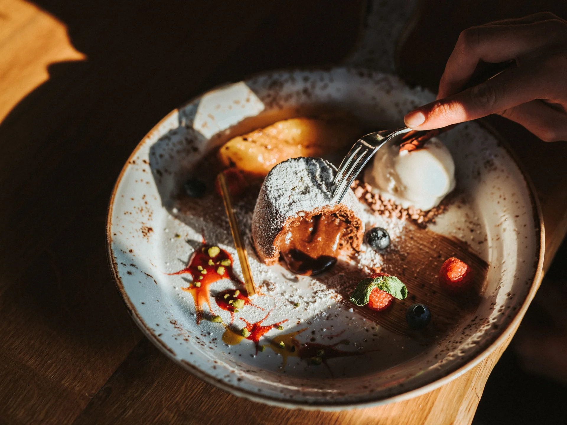 Bilder, die Sie sehen müssen. Hand hält Gabel, nimmt warmen Schokokuchen mit Beeren und Eis vom Teller